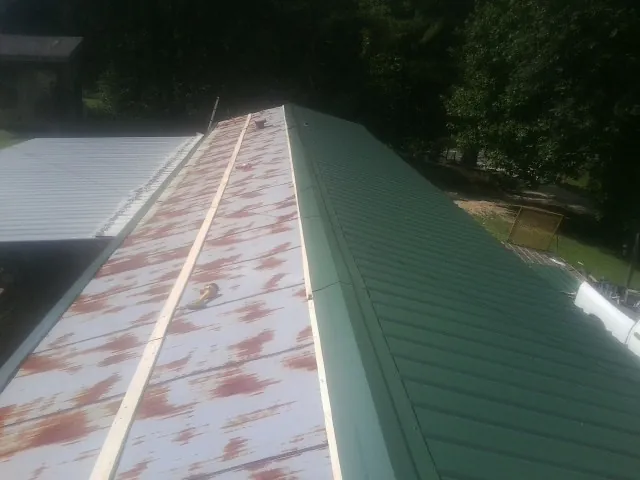 Old rusted panels beside newly installed green metal roofing — Wind Damage Roof Repair by Roofing Brothers in Nickelsville