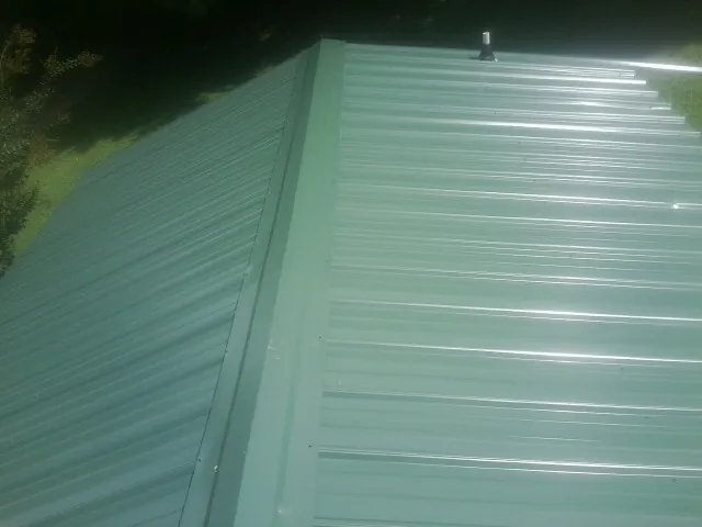 New green metal panels meeting at the ridge of a roof — Flat Roof Repair work by our crew in Nickelsville