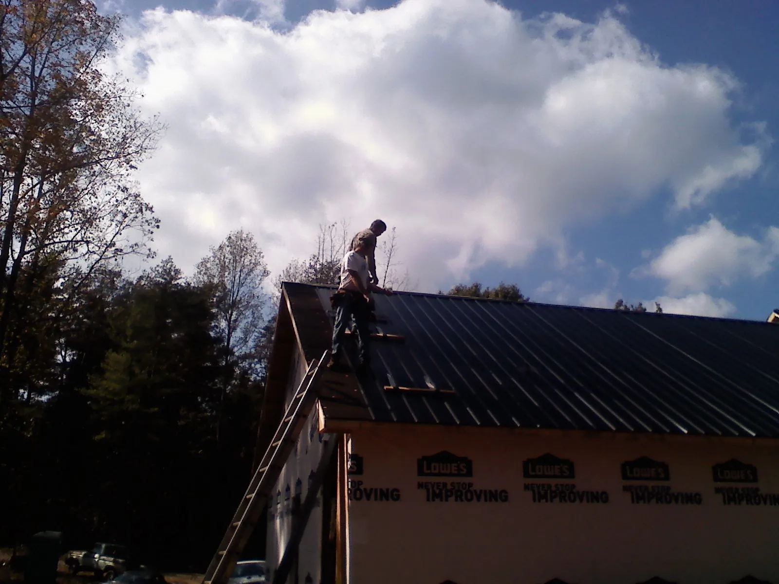 Roofer fastening dark metal panels high against a cloudy sky, from a Roof Inspection job in Nickelsville