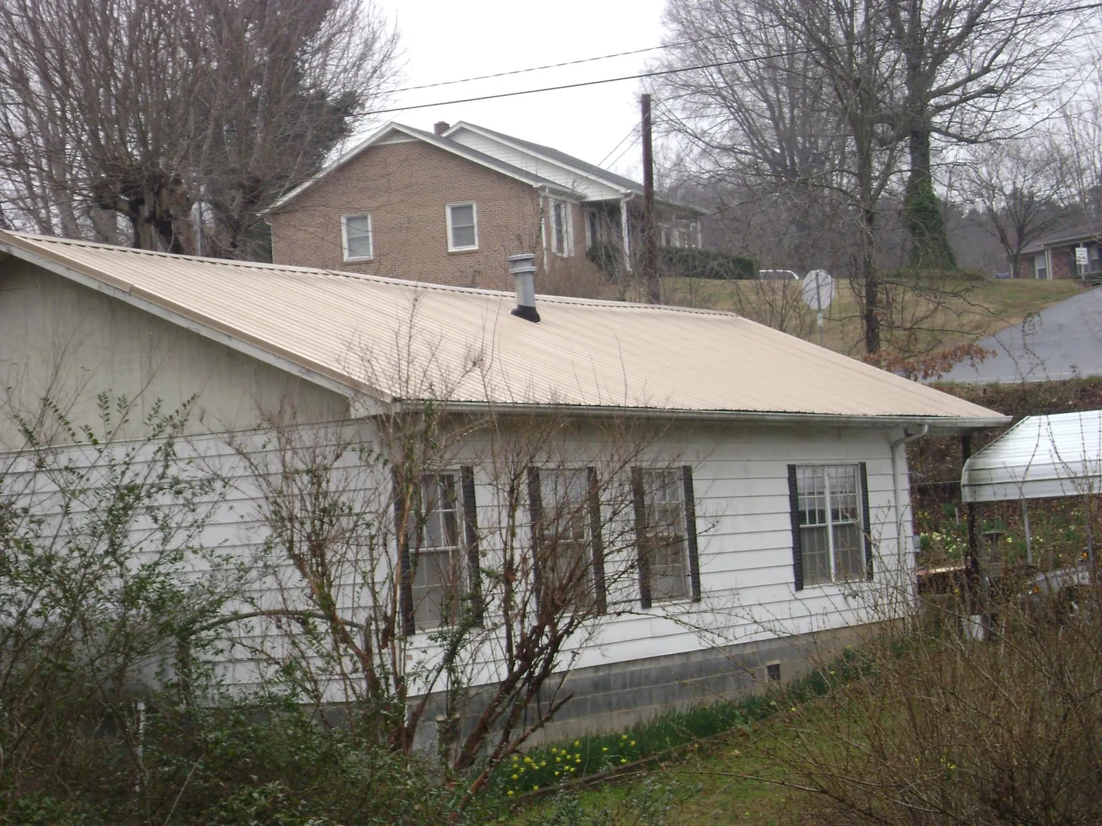 Tan metal roof on a white sided house set into a hillside — Commercial Roofing by Roofing Brothers in Nickelsville